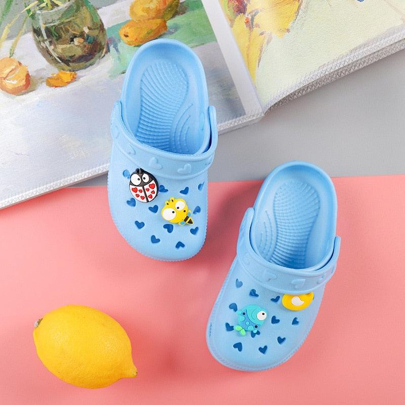 Blue children's clogs with cartoon designs on a pink surface with a lemon.