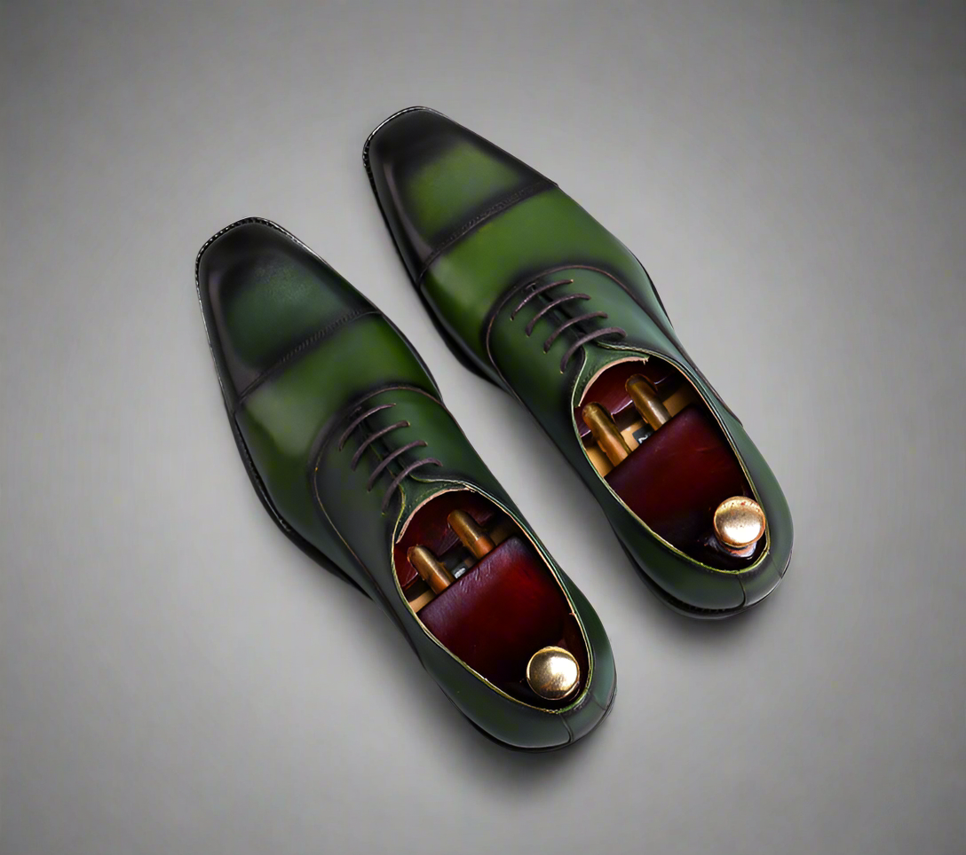 Green leather dress shoes with gold accents on a gray background