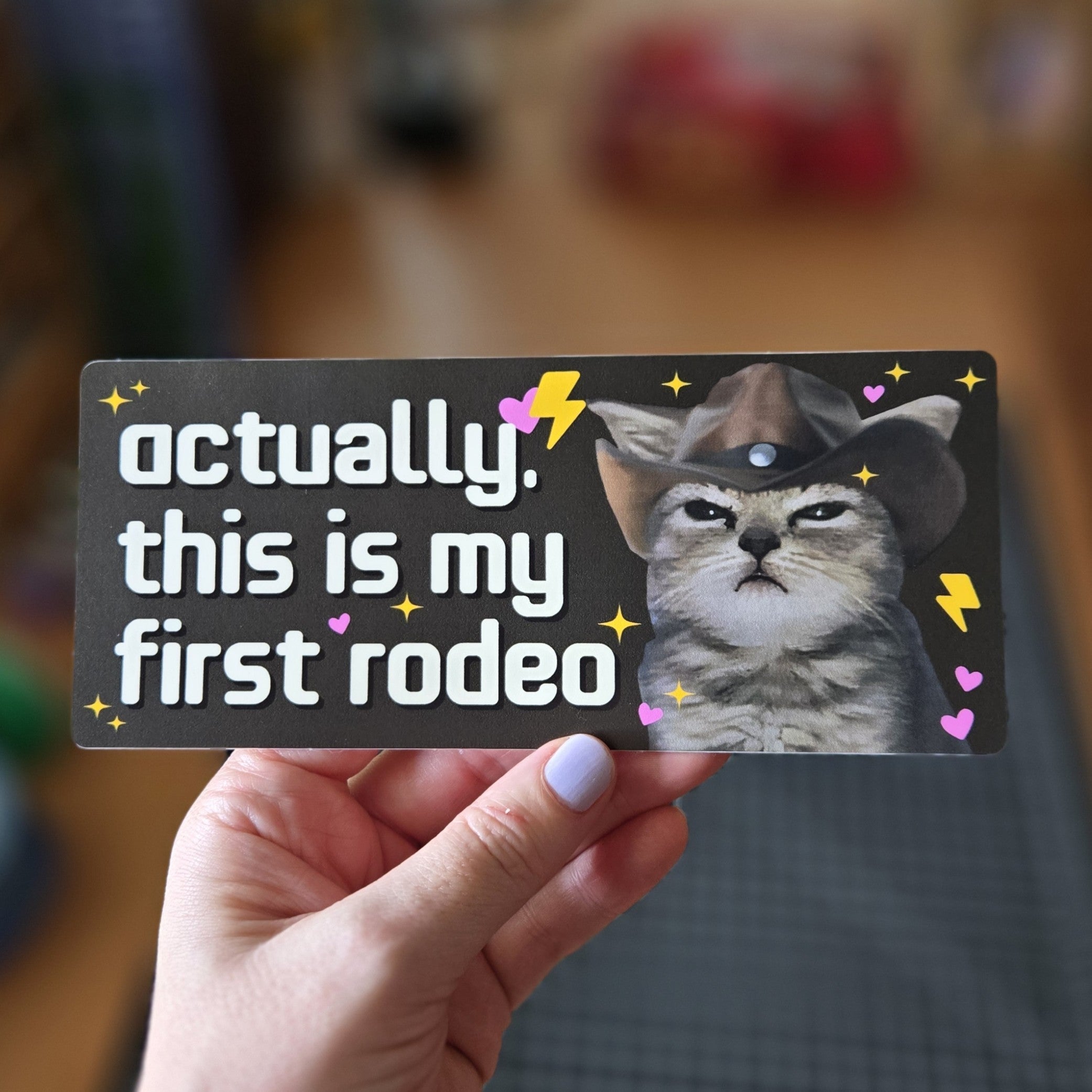 Card with a cat wearing a cowboy hat and text 'Actually, this is my first rodeo' held by a hand.