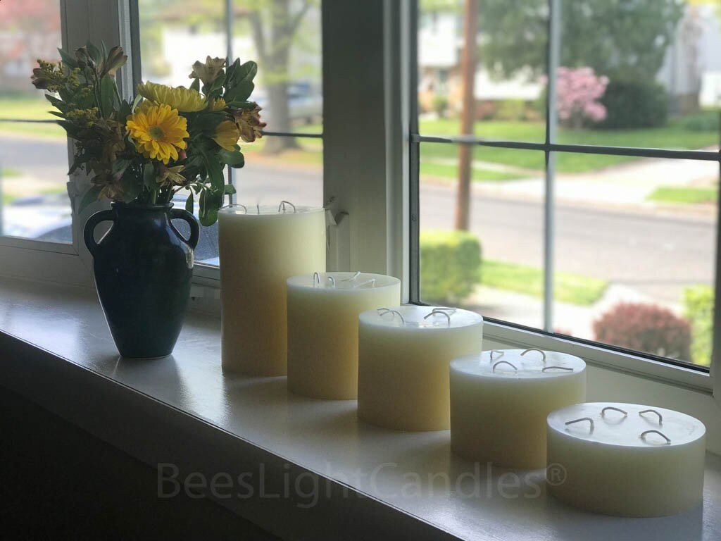 Set of candles on a windowsill with a vase of flowers, visible 'BeesLight Candles' branding.