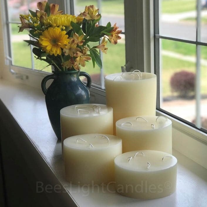 Set of five white candles on a windowsill with a vase of yellow flowers.