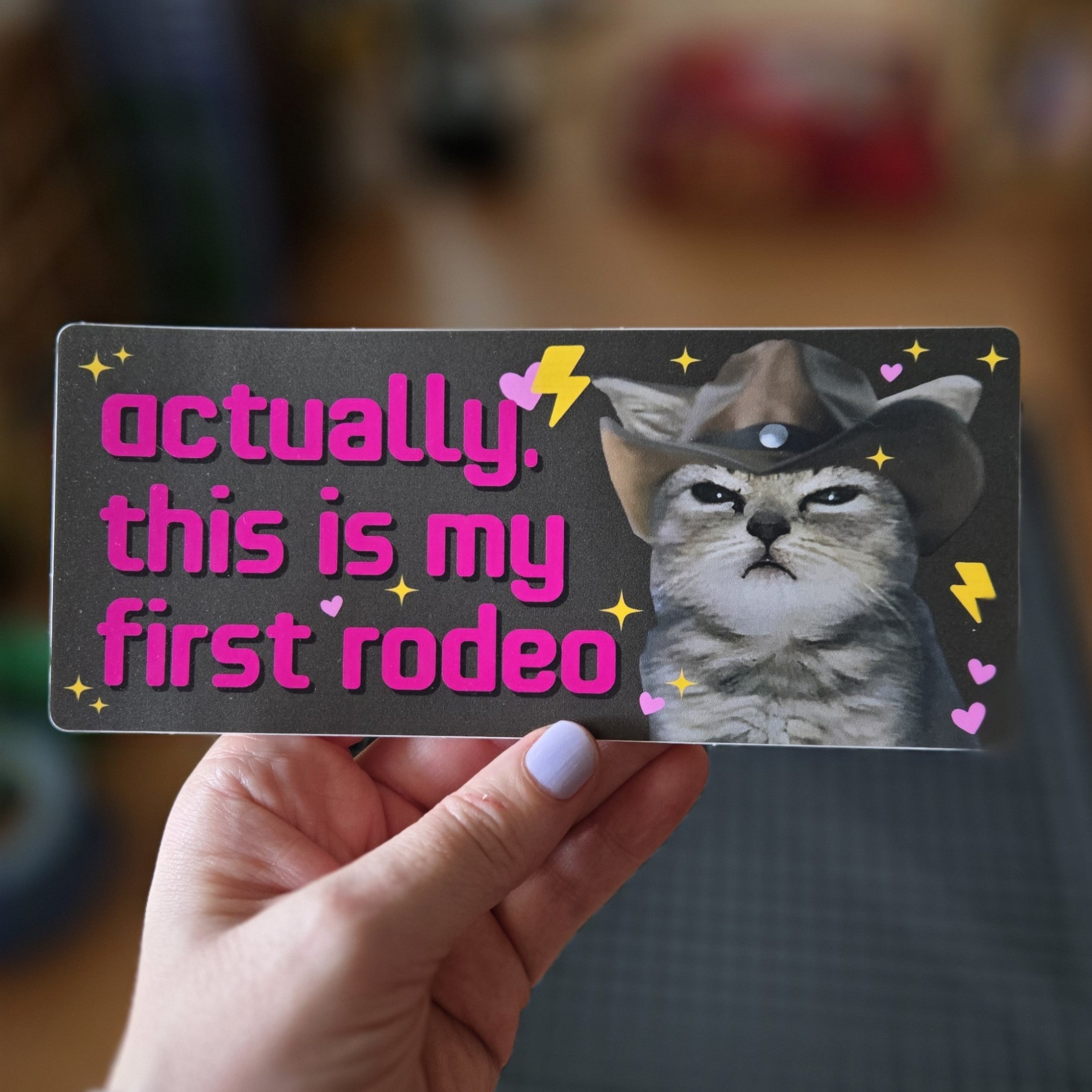 Card with a cat wearing a cowboy hat and text 'actually, this is my first rodeo' held by a hand.