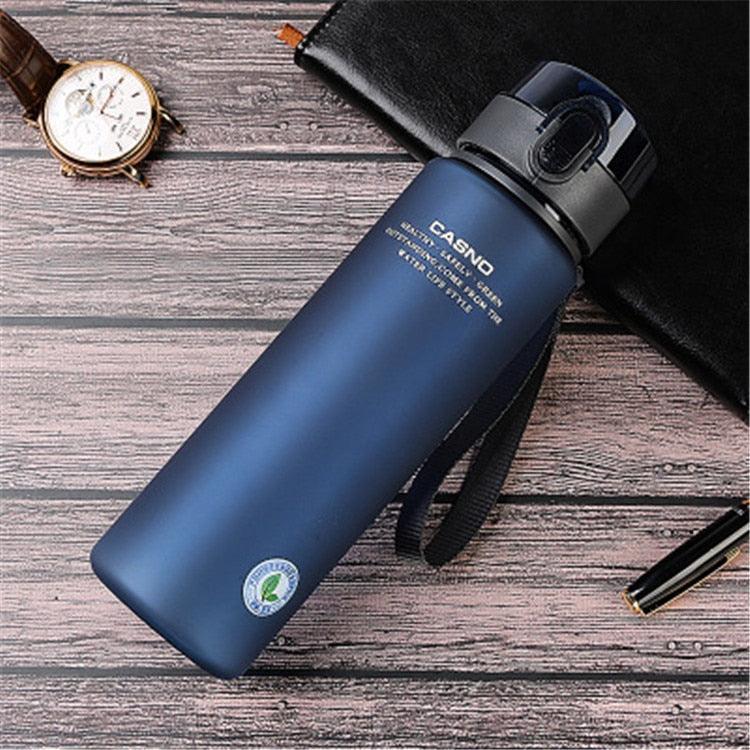 Blue water bottle with a black lid on a wooden surface, next to a watch and pen.