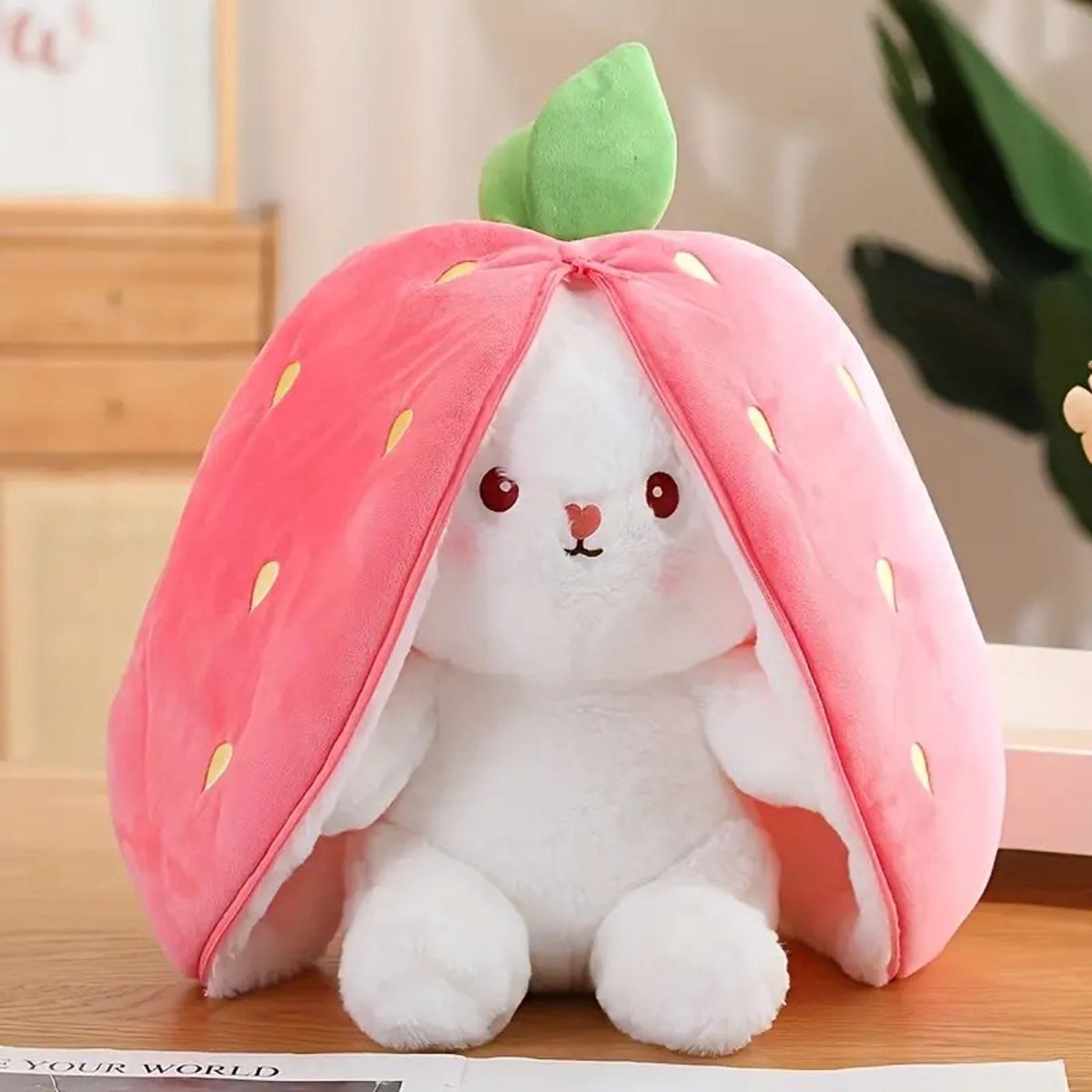 Plush toy shaped like a strawberry with a white rabbit inside on a wooden surface.