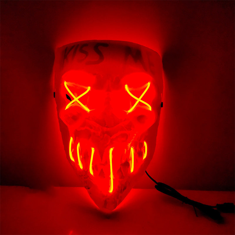 A red skull-shaped LED light mask with glowing yellow eye and mouth details, shown illuminated against a dark red background.