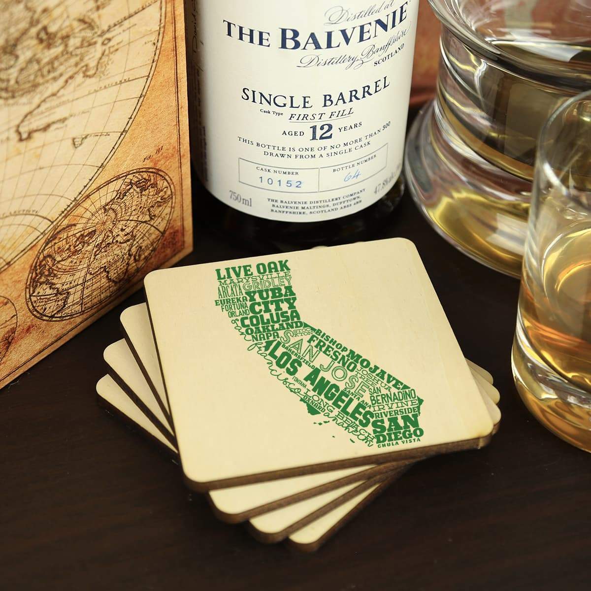 Balvenie whisky bottle with coasters featuring city names on a wooden surface