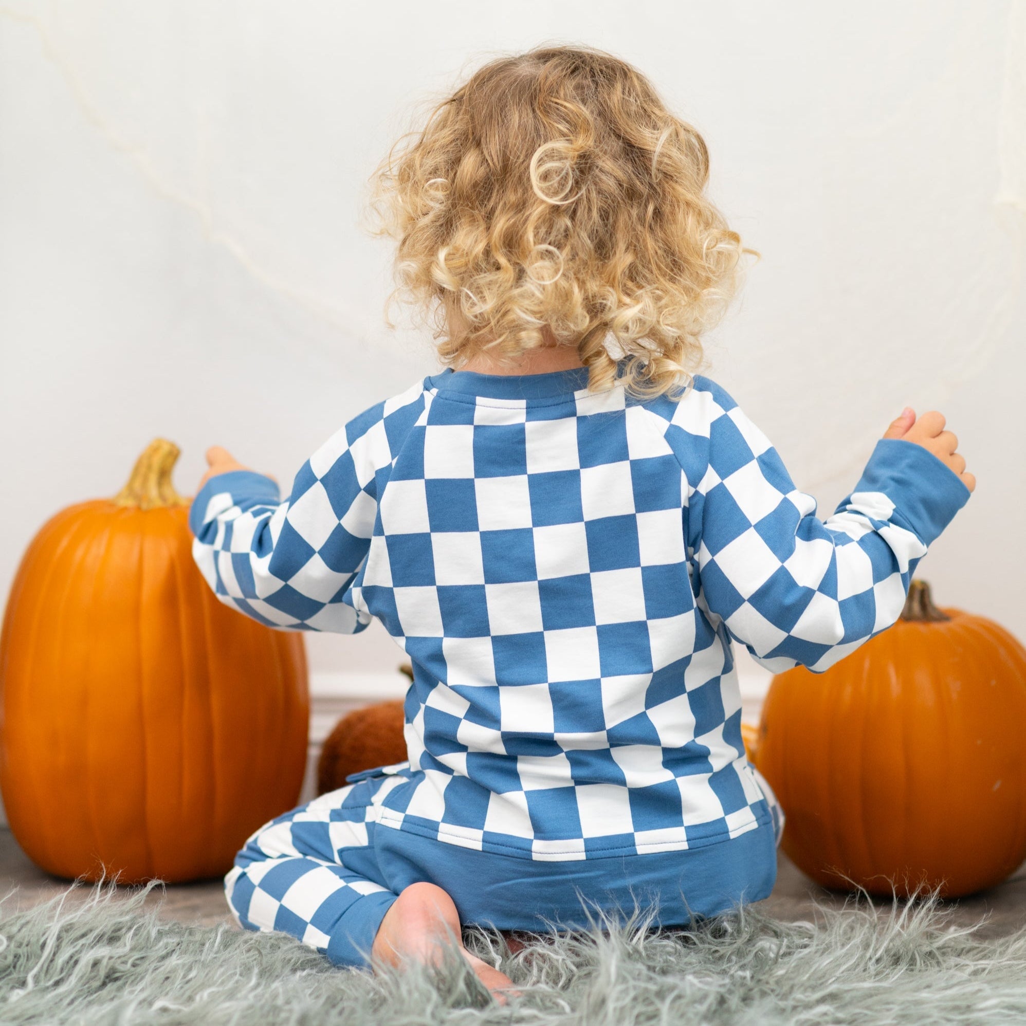 Child wearing a blue and white checkered outfit with pumpkins in the background
