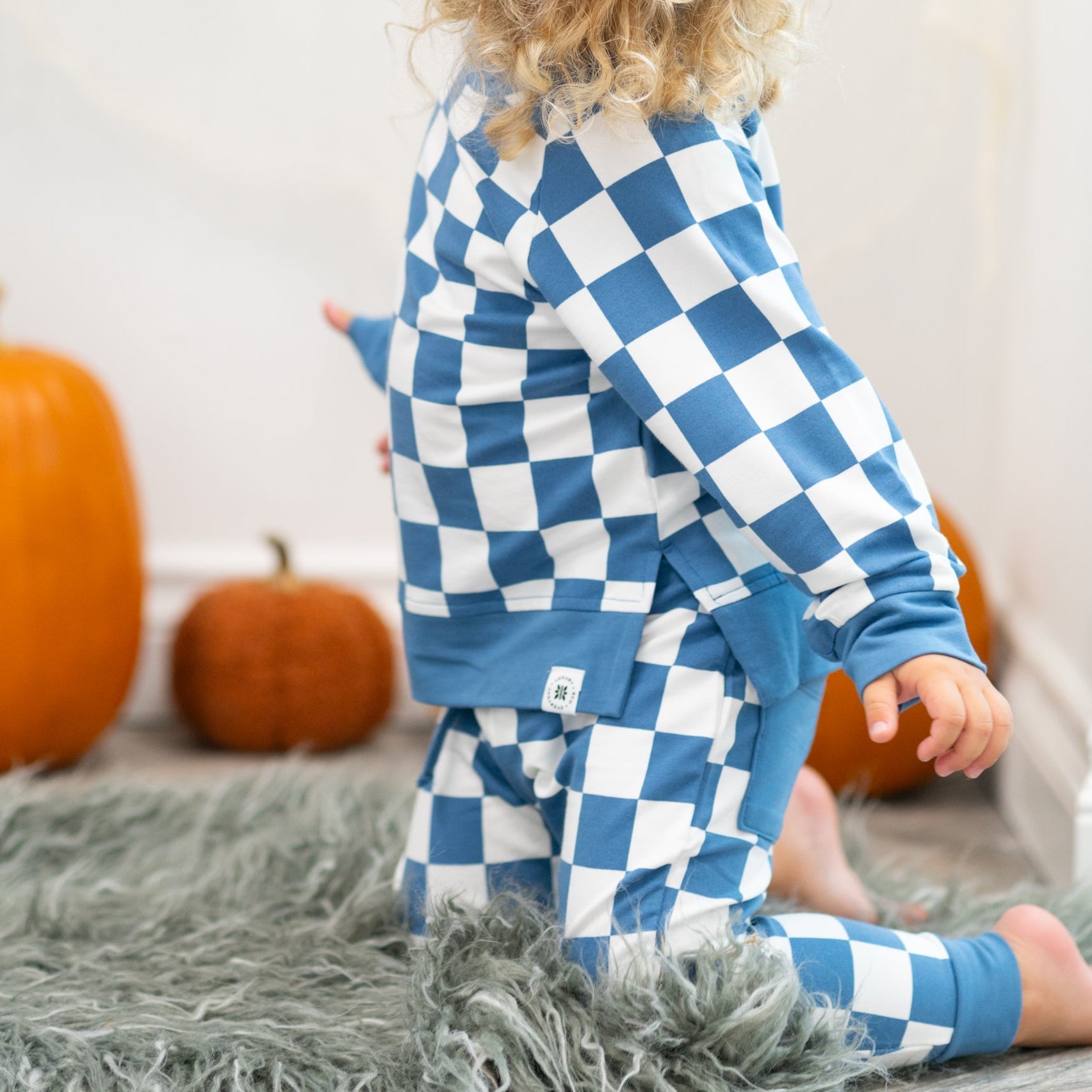 Child wearing blue and white checkered pajamas with pumpkins in the background.