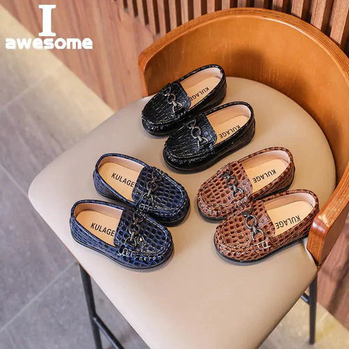 three pairs of croc-embossed leather loafers for toddlers in black, navy blue, and auburn/brown, with a metal chain detail and slip-on style, displayed on a chair.