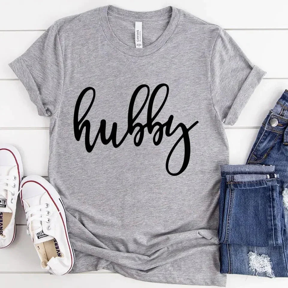 Gray t-shirt with 'hubby' text, paired with jeans and sneakers on a light wooden surface.