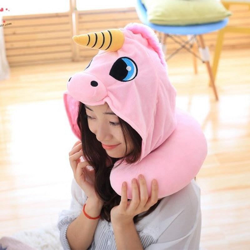 Person wearing a pink unicorn-shaped neck pillow in a room with wooden floor and chair.