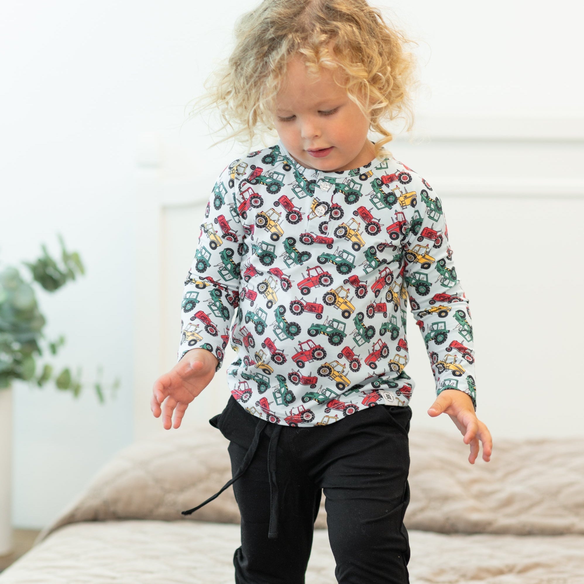 Child wearing a long-sleeve shirt with colorful tractor pattern in a home setting.