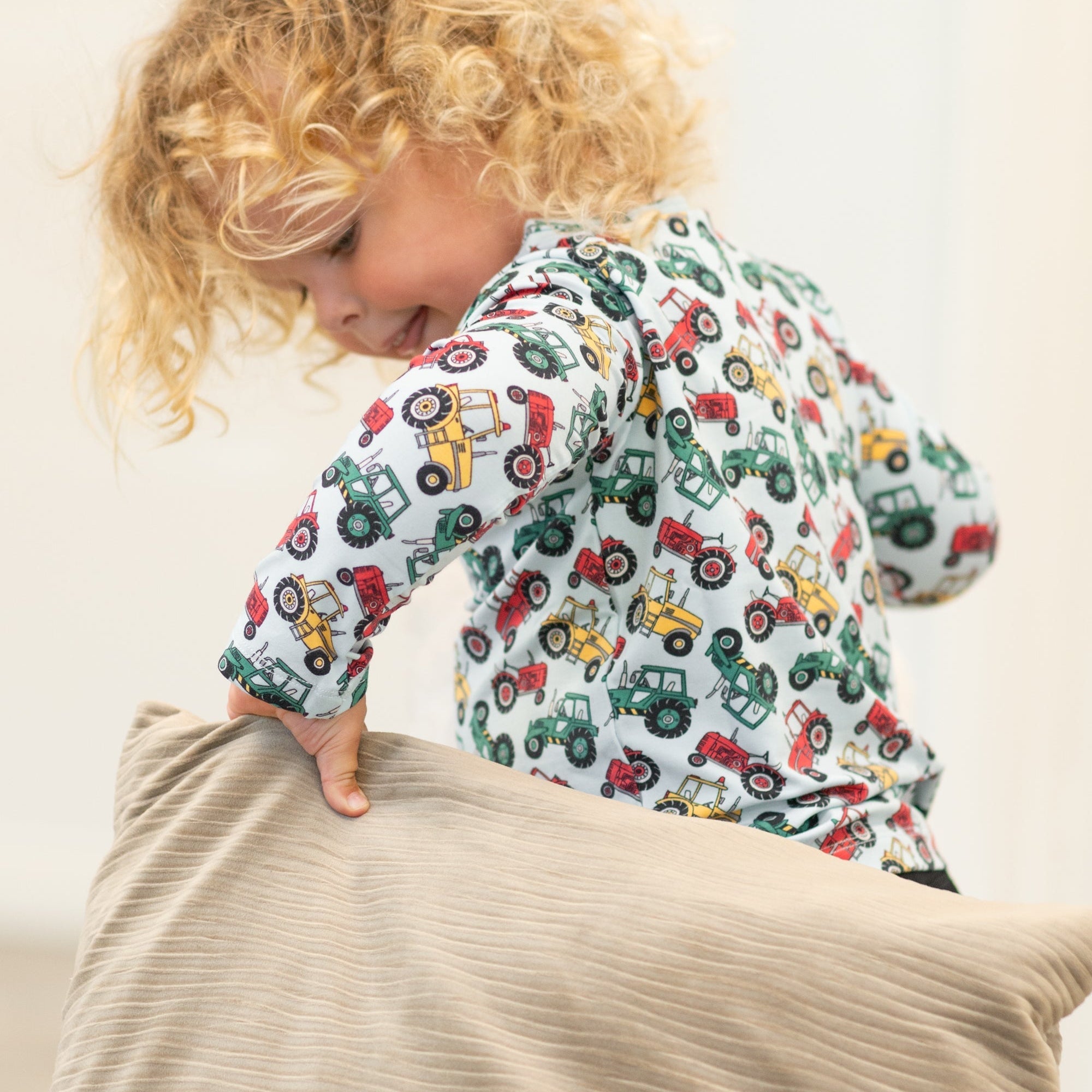 Child wearing a long-sleeve shirt with tractor pattern, sitting on a beige surface.