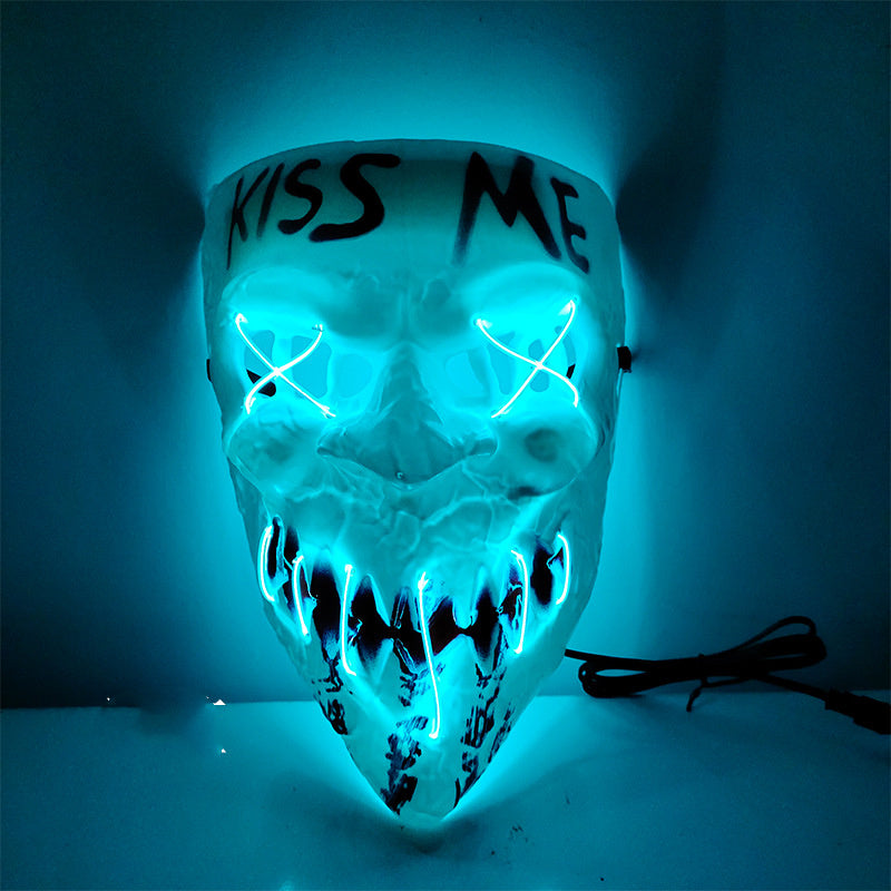 A skull-shaped LED light mask with glowing blue eyes, sharp teeth, and the words 'KISS ME' written on the forehead, shown against a dark blue background.