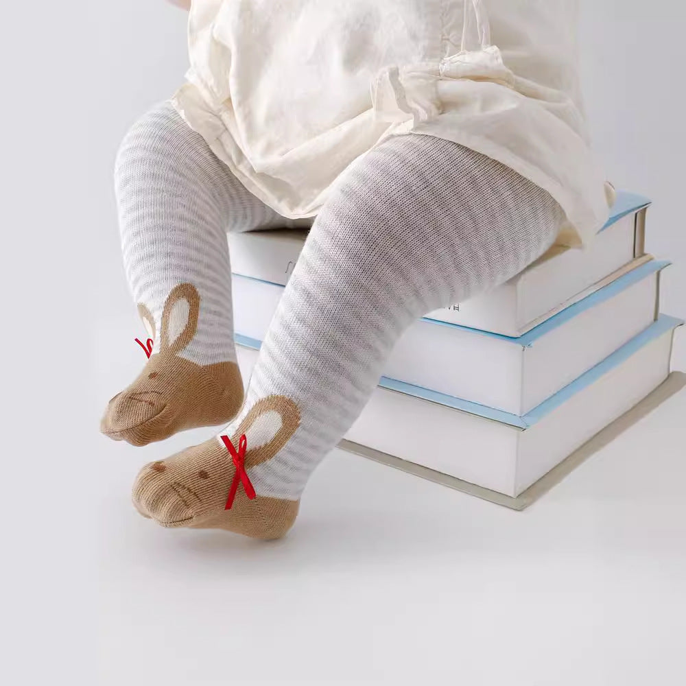 Baby wearing striped tights and bunny socks with red bows, standing on stacked books.