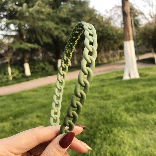 Green braided hairband held by a hand with a blurred park background