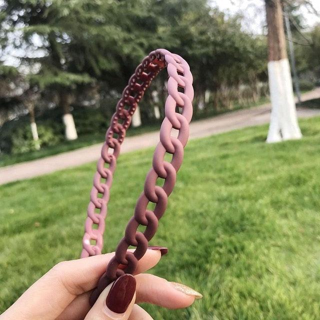 Pink woven headband held by a hand with a blurred green outdoor background