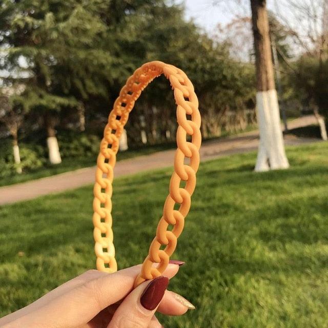 Orange chain-shaped object held by a hand with a park background
