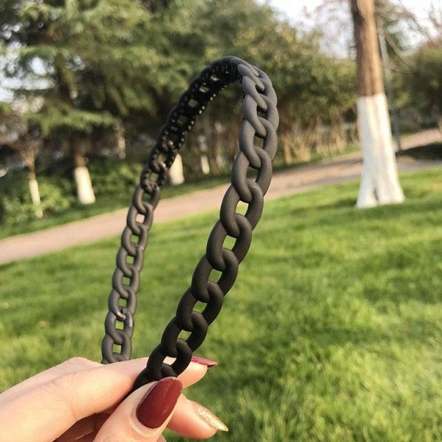 Black braided hairband held by a hand with a blurred park background