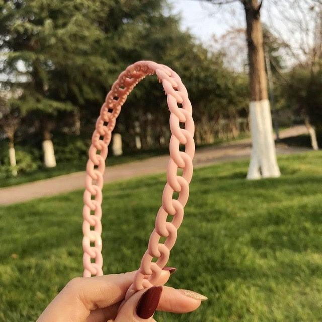 Pink chainlink object held by a hand with a park background
