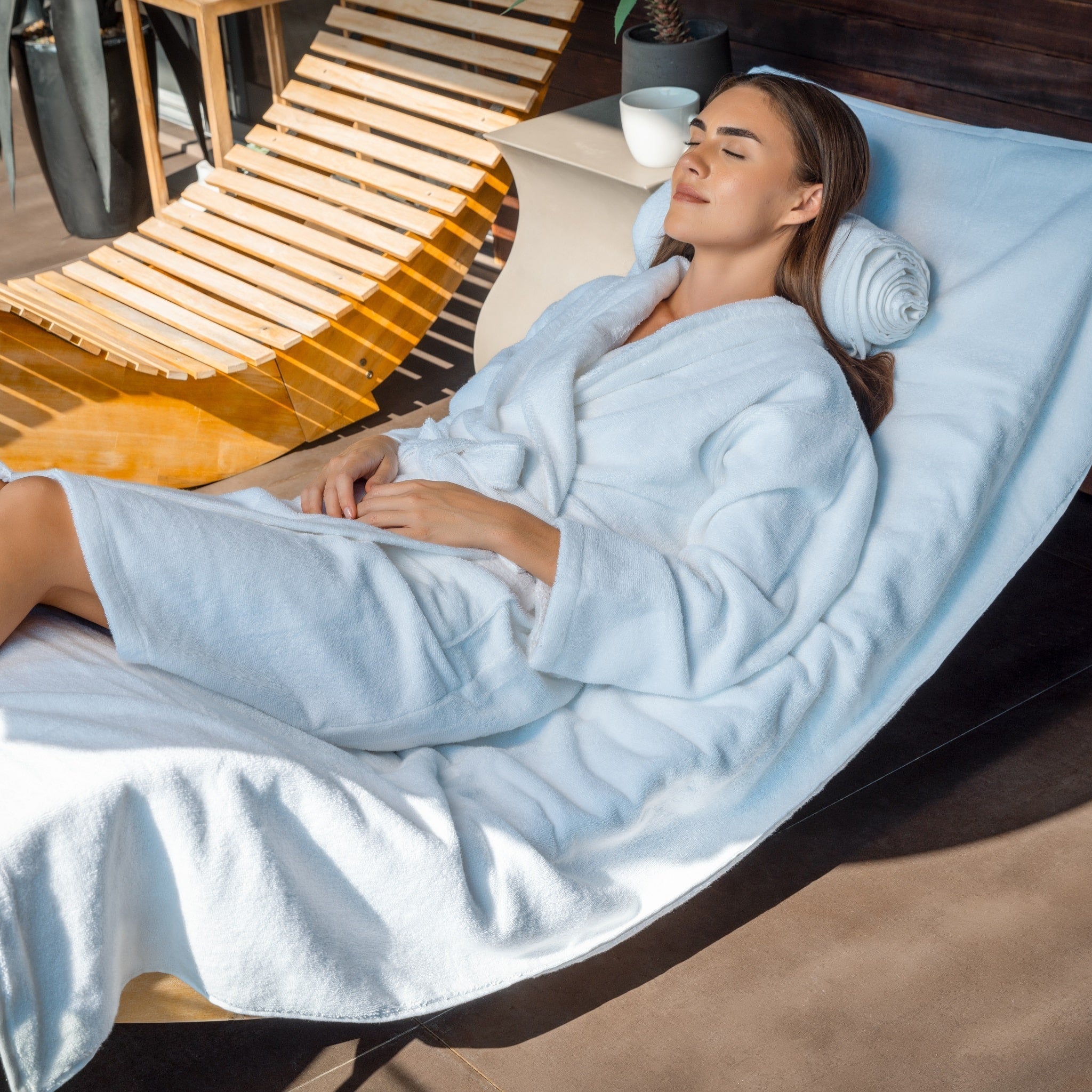 Woman in a light blue robe lying on a modern lounge chair with a wooden backrest.
