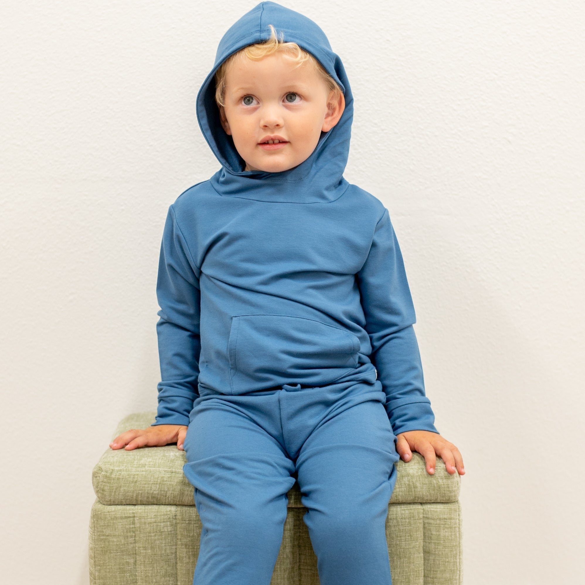 Child wearing a blue hoodie and pants sitting on a green chair against a white background