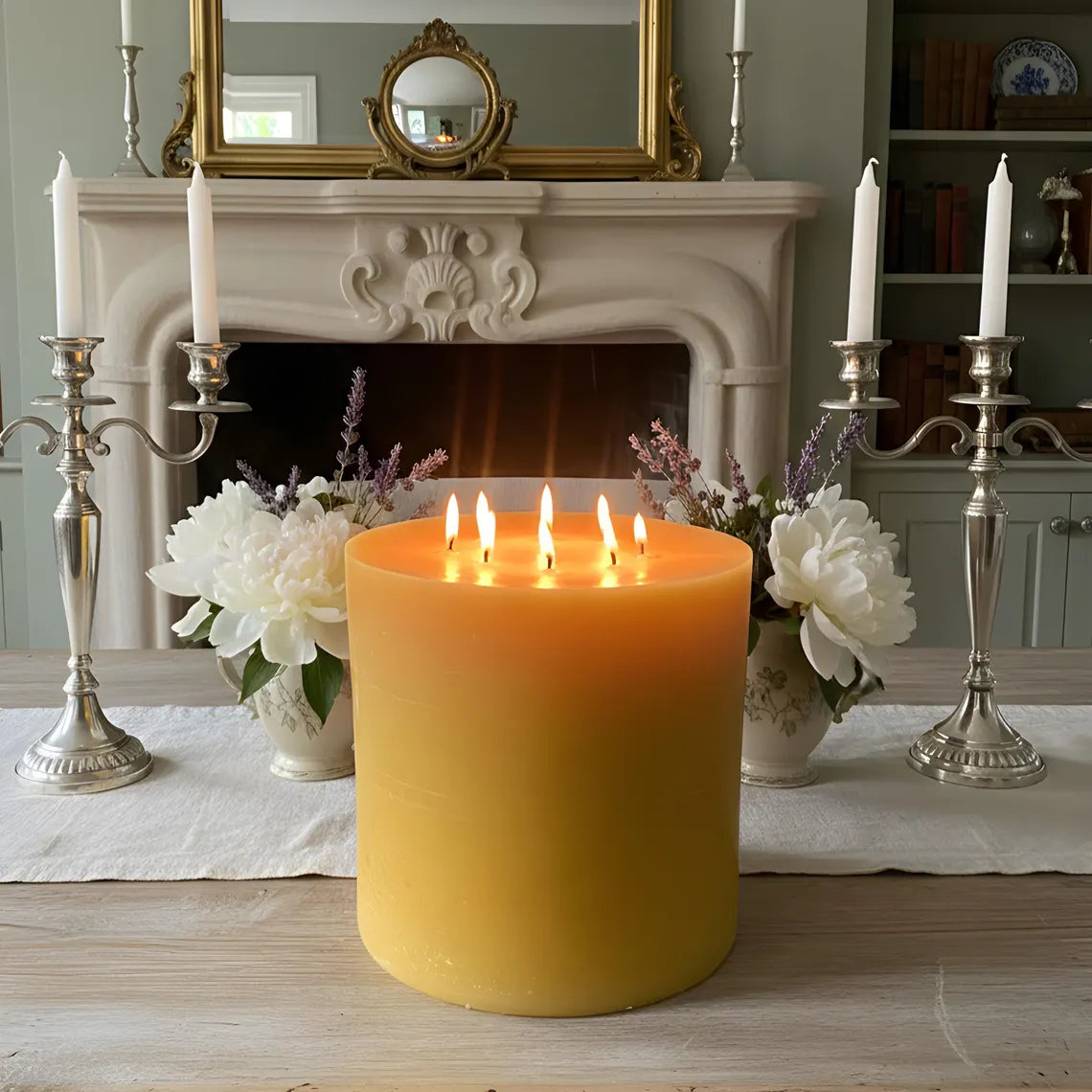 Large candle with three flames on a table in front of a fireplace with decorative elements.