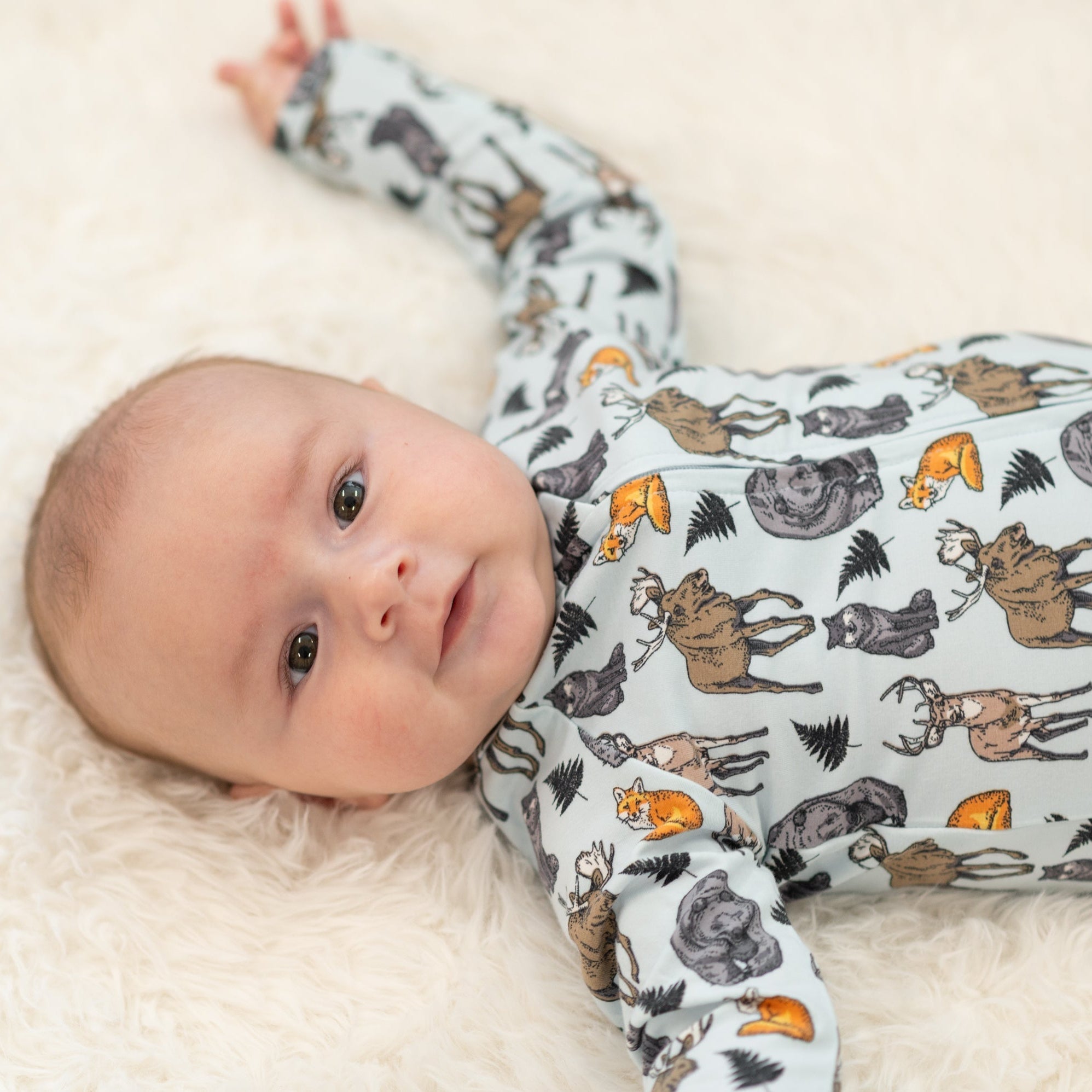Baby wearing a onesie with animal patterns on a soft surface