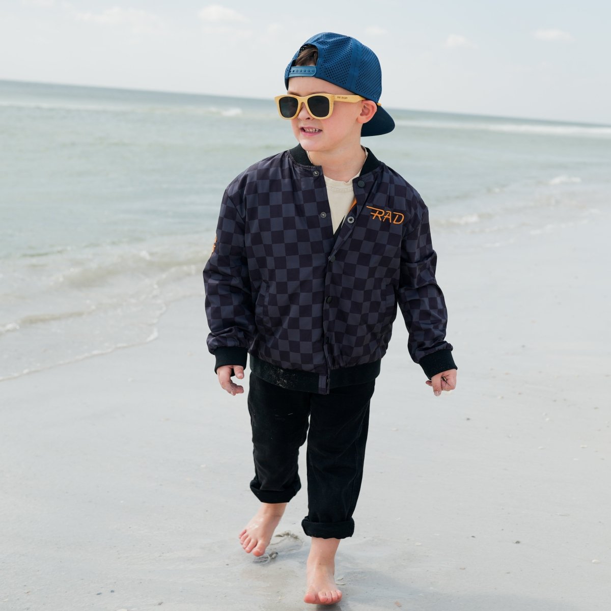 Child wearing a checkered jacket and sunglasses on a beach