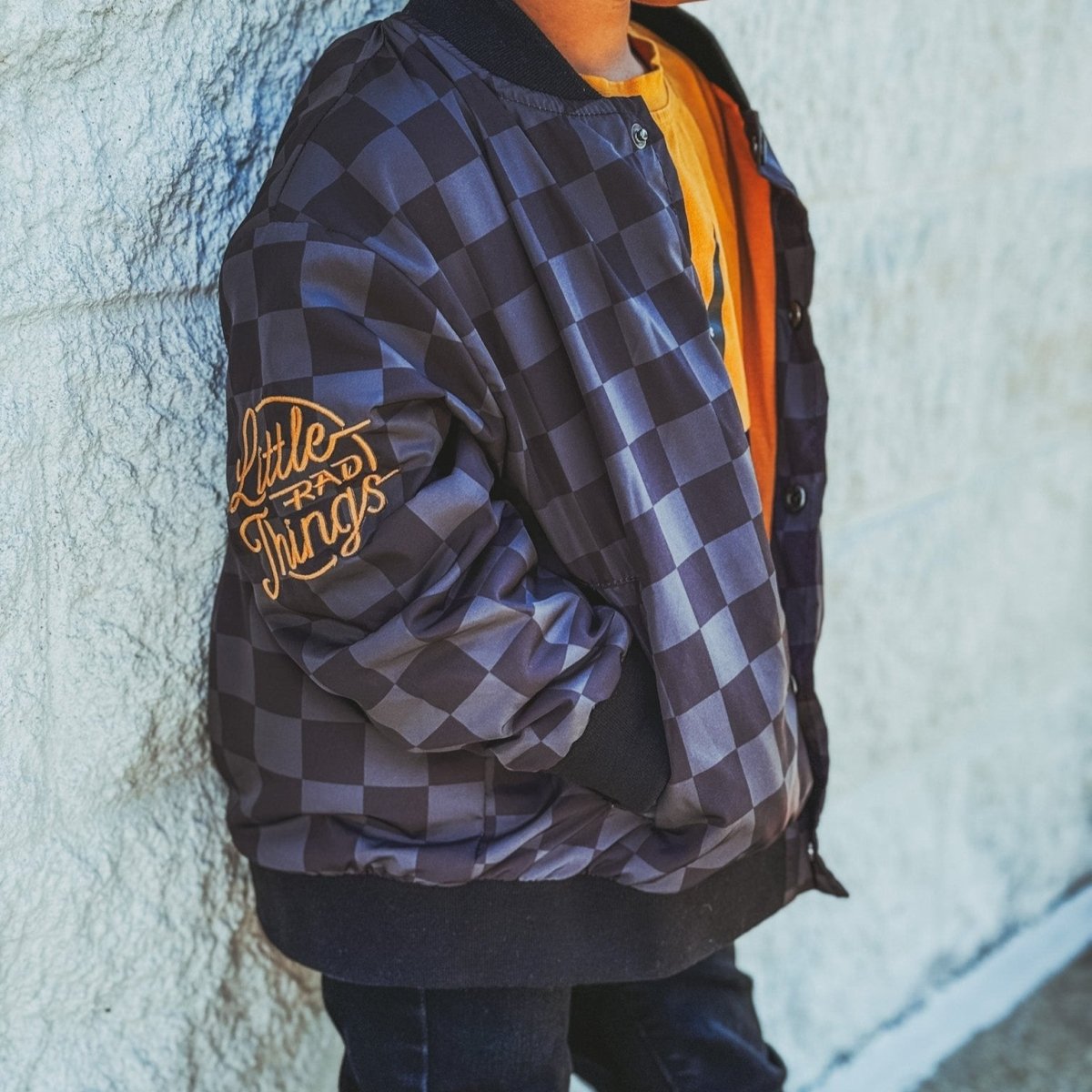 Person wearing a checkered jacket with 'Little Things' text against a textured wall.