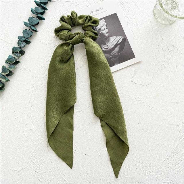 Green scrunchie with a ribbon on a textured white surface with decorative elements.