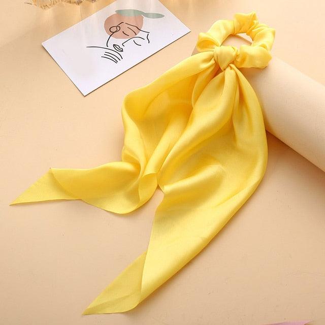 Yellow scarf tied as a hair accessory on a beige surface with a small drawing in the background.