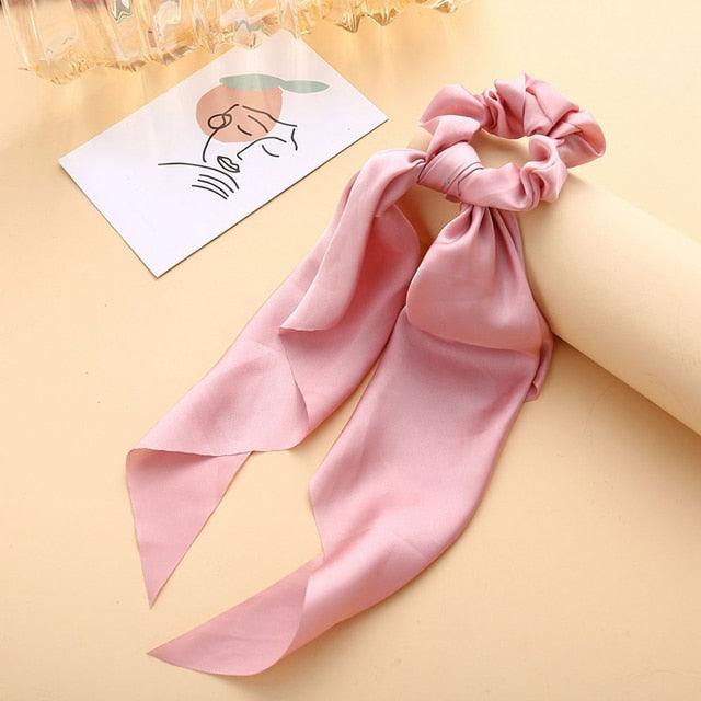 Pink hair scarf and scrunchie on a beige surface with a small drawing in the background.