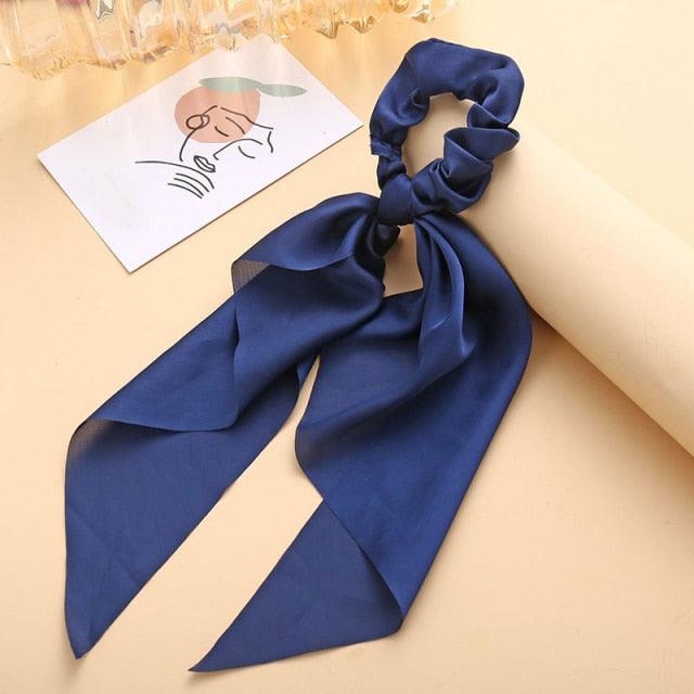 Blue hair scrunchie with a long silk ribbon on a beige surface