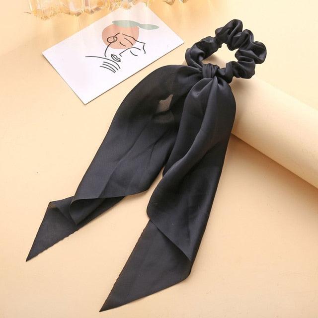 Black hair scrunchie with a ribbon on a beige surface