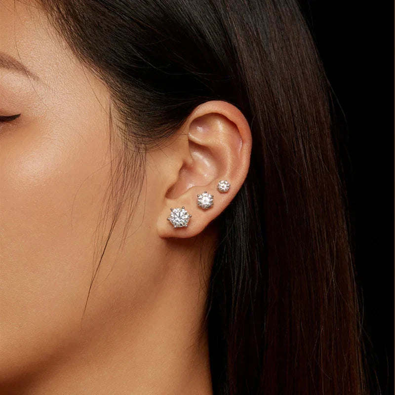 Close-up of an ear wearing three diamond stud earrings with a dark background