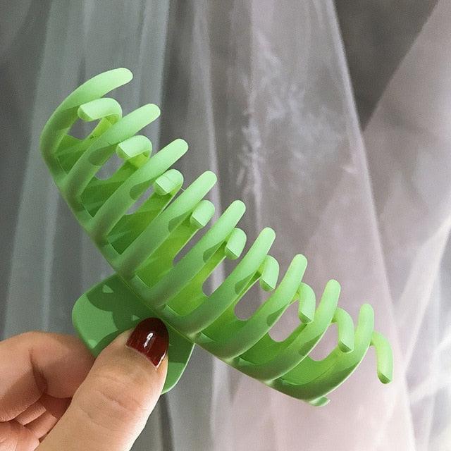 Green hair styling tool held by a hand against a neutral background