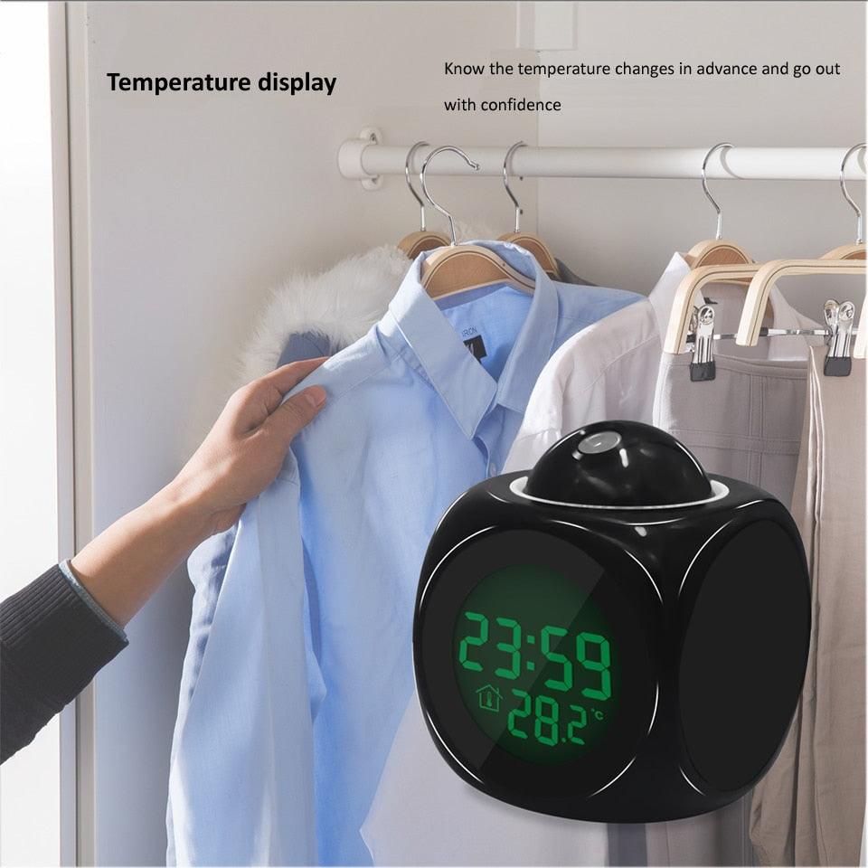 Digital clock with temperature display in front of hanging shirts