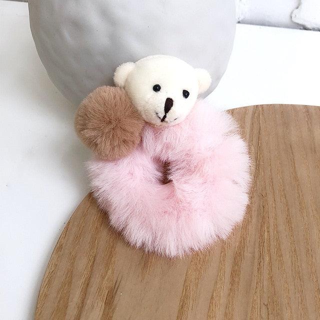 Small white teddy bear with pink fluffy skirt and brown pom-pom on a wooden surface