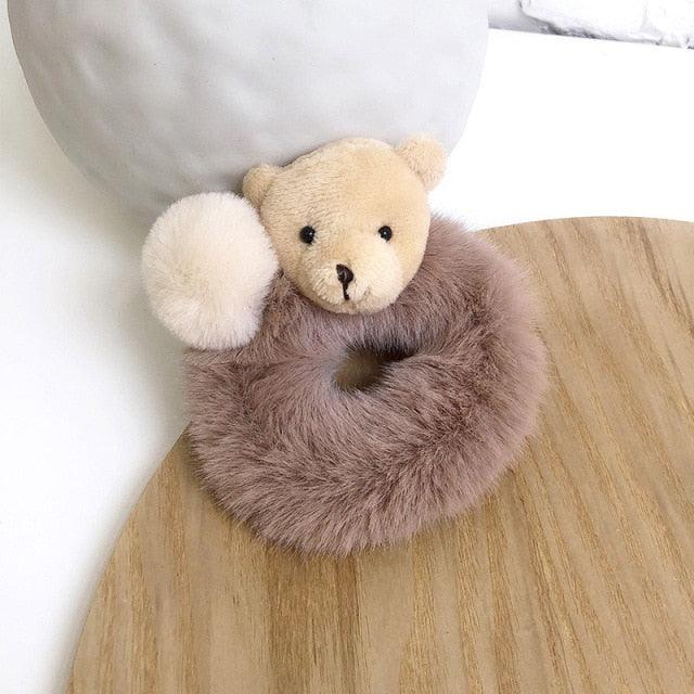 Plush teddy bear with a fluffy brown ring on a wooden surface
