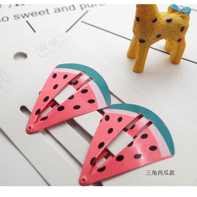 Watermelon slice hair clips on a white surface with a small toy in the background