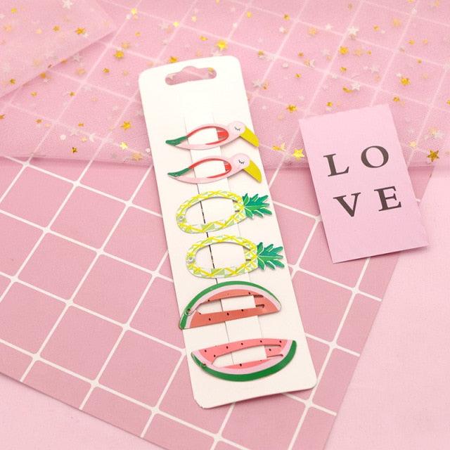 Packaged hair clips with fruit designs on a pink grid background