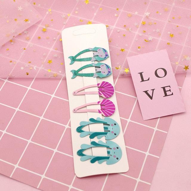 Set of colorful hair clips on a pink grid background with a 'LOVE' card.