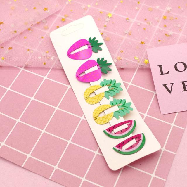 Colorful fruit-shaped hair clips on a pink grid background