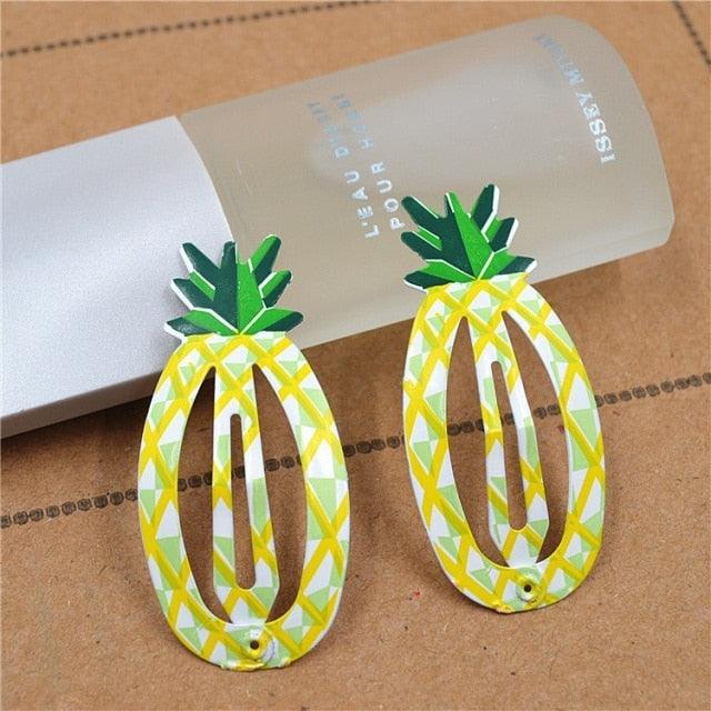 Pineapple-shaped earrings on a brown surface with a cylindrical object in the background.