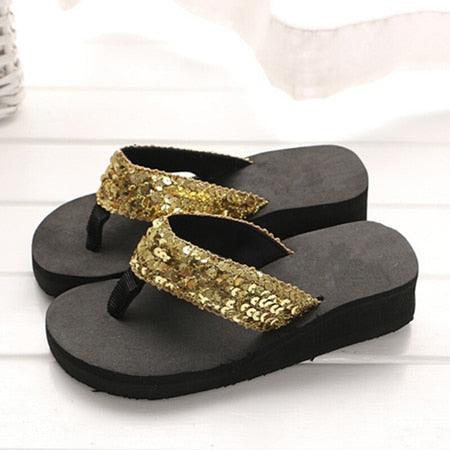 Black sandals with gold sequin straps on a white background