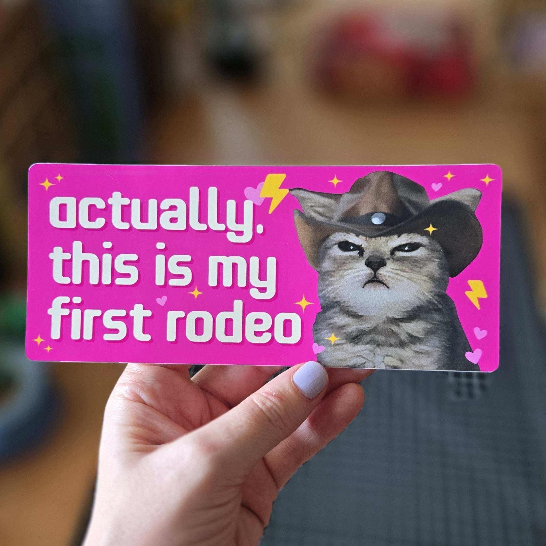 Card with a cat wearing a cowboy hat and text 'Actually, this is my first rodeo' held by a hand.