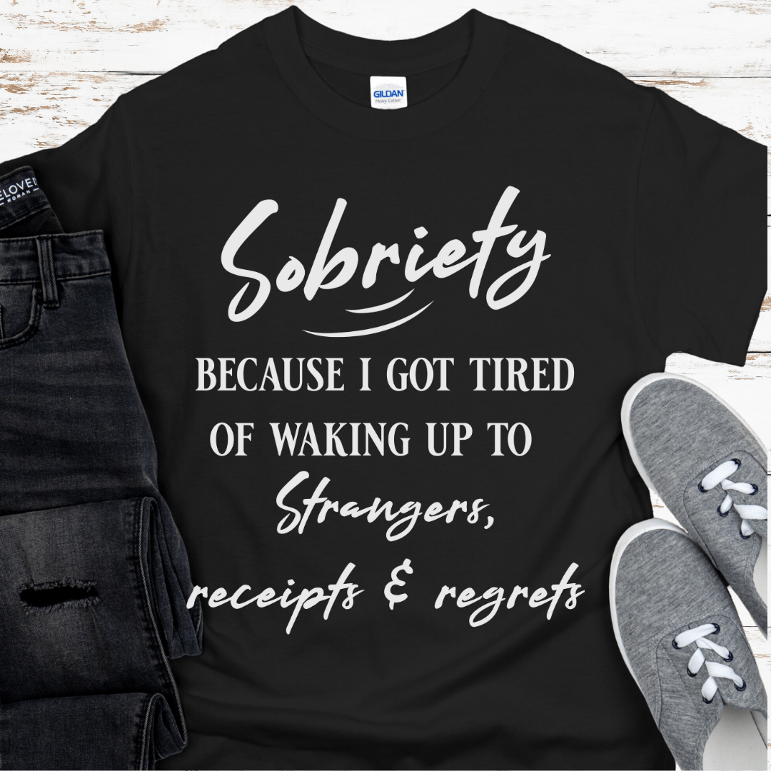 Black t-shirt with white text on a wooden surface with jeans and sneakers.