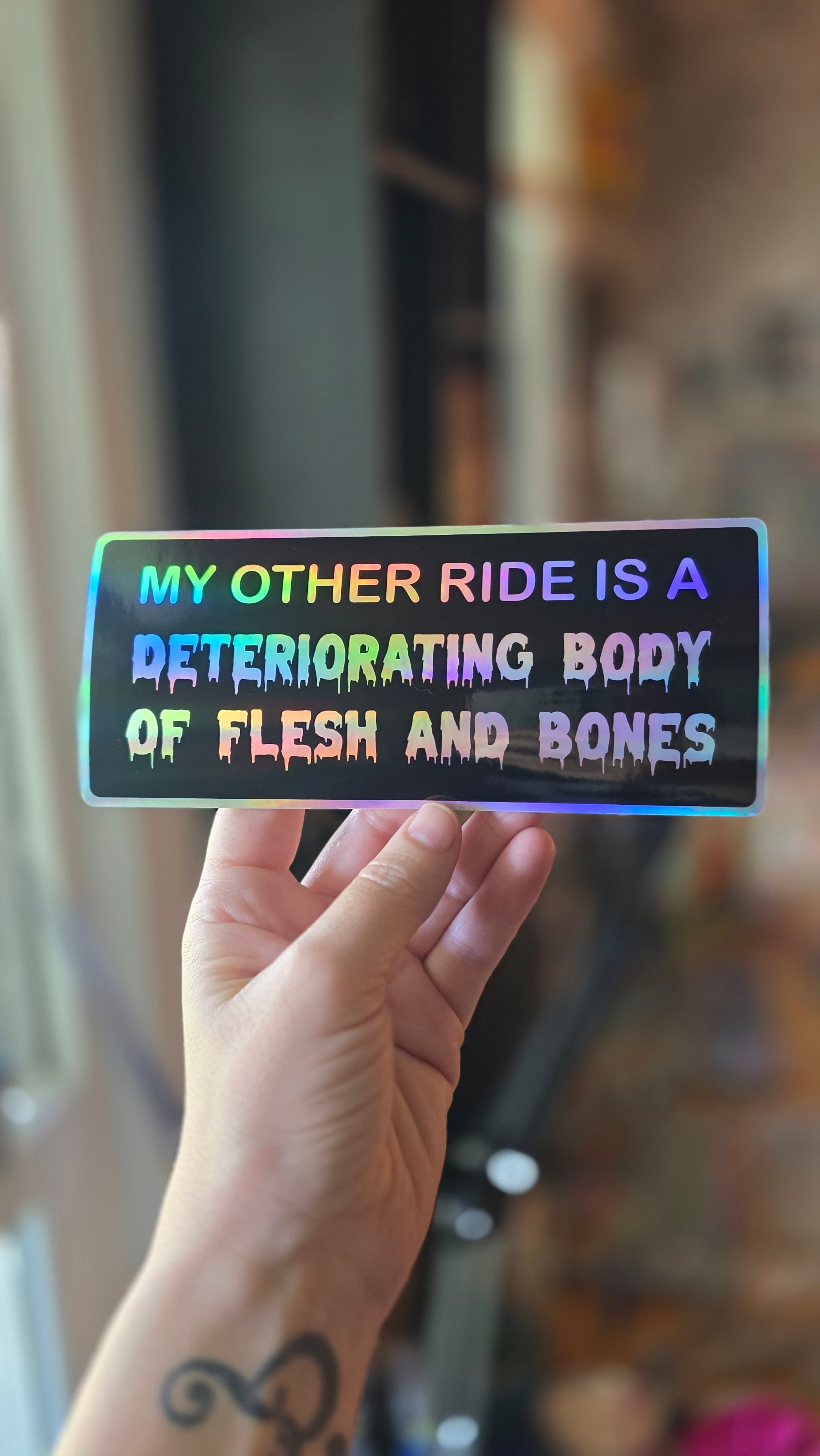 Holographic sticker with text held by a hand against a blurred background