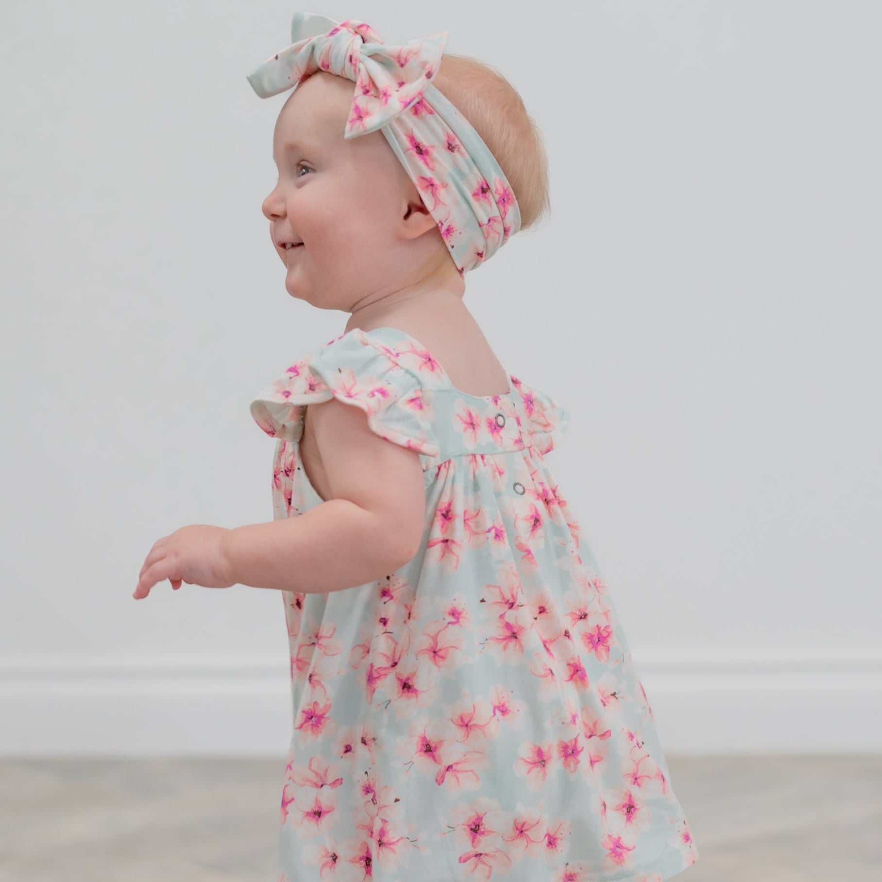 Baby wearing a floral dress and headband on a plain background